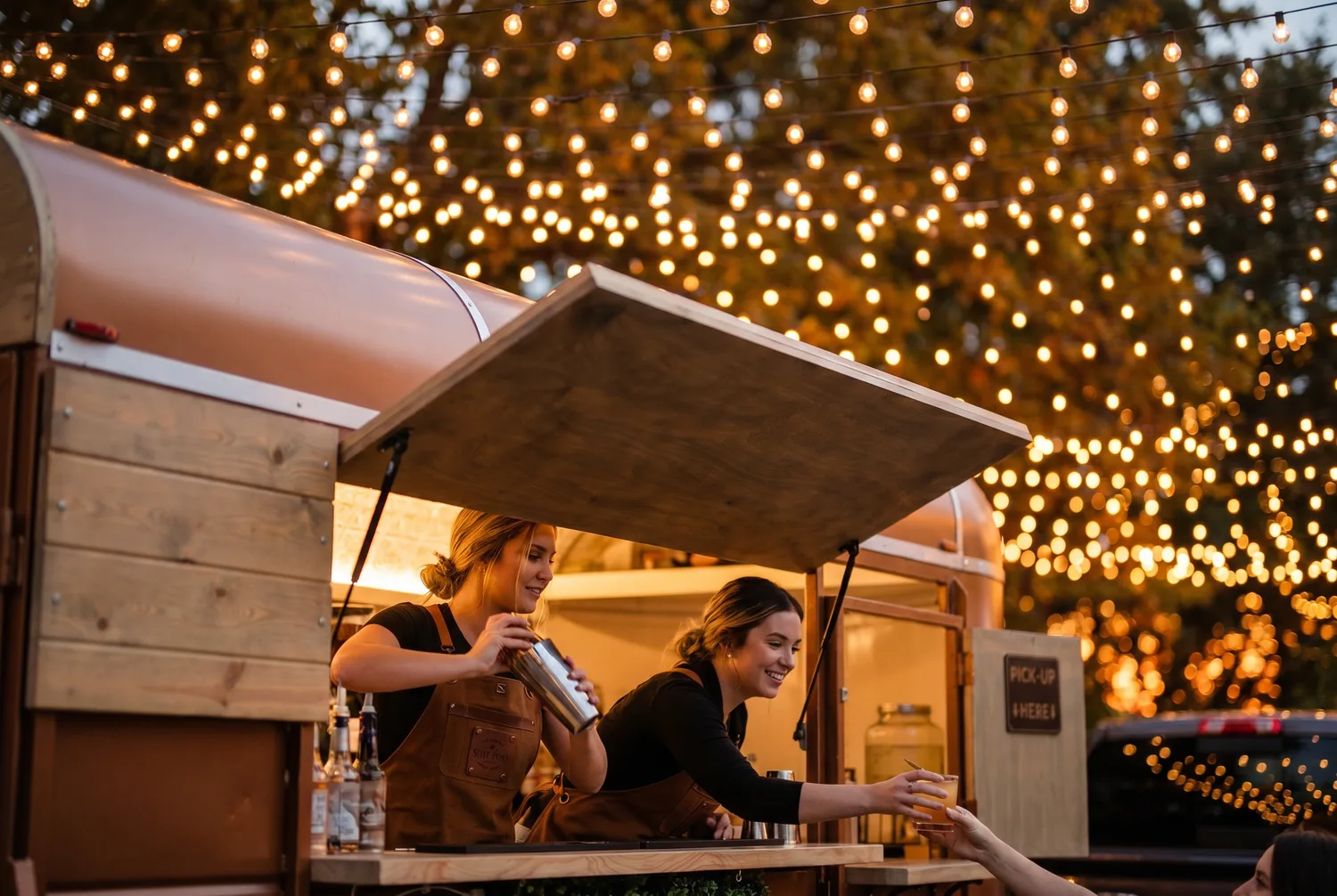 Steel Pony baristas serving from the trailer under string lights at an evening event