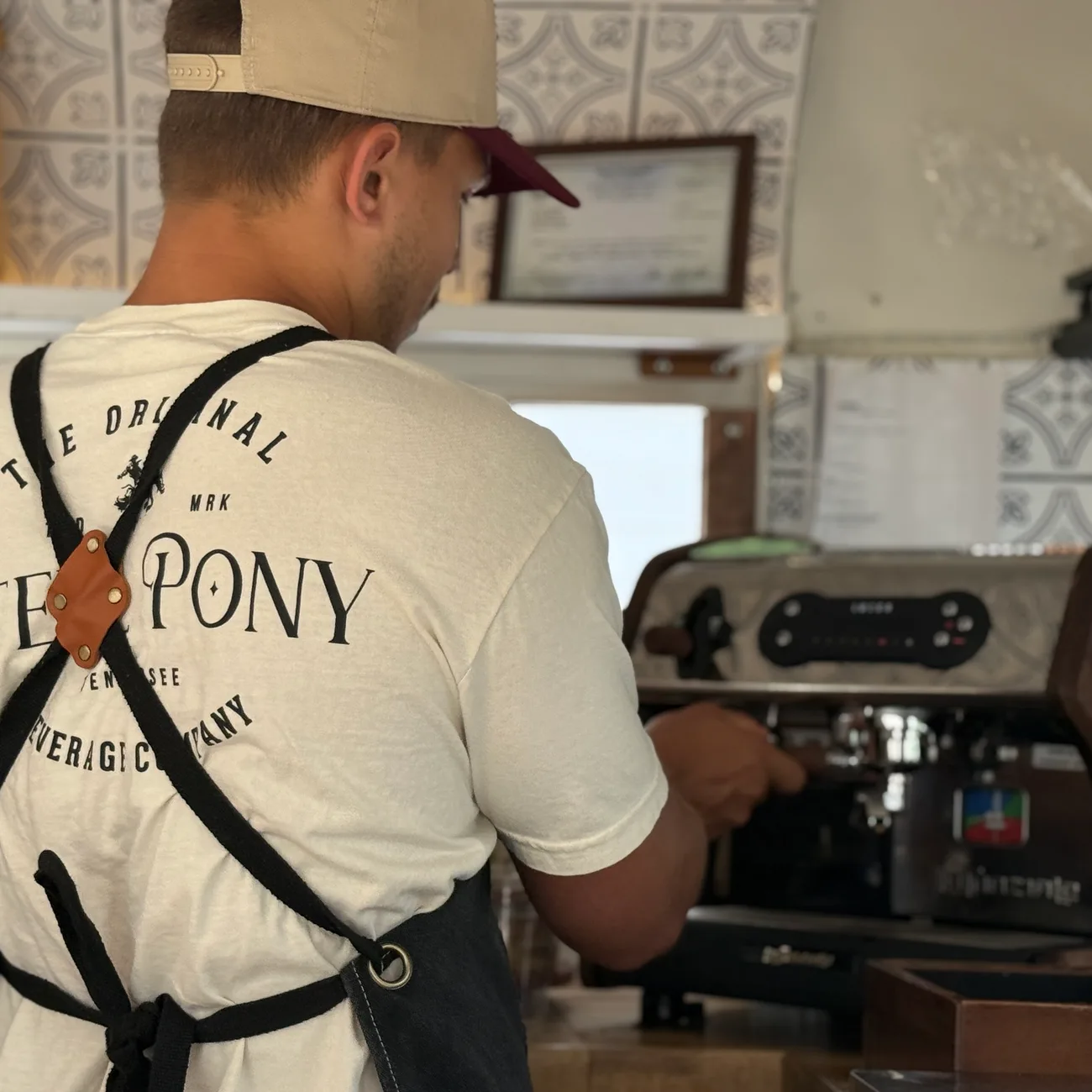 A Steel Pony barista in a branded tee pulling shots at the espresso machine