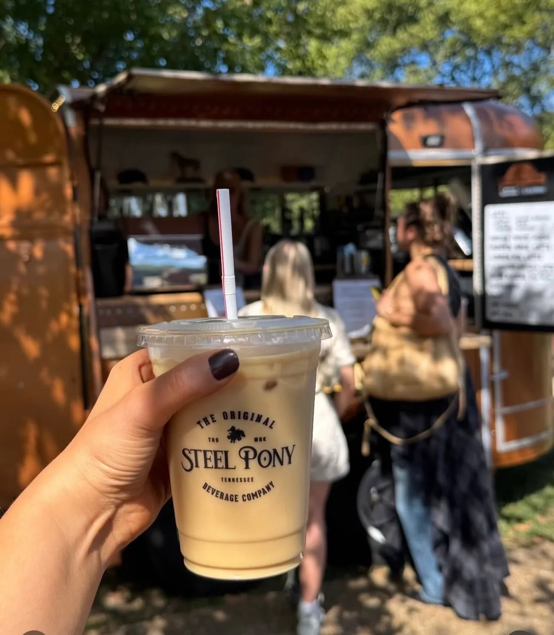 A guest holding a branded Steel Pony iced drink in front of the trailer cafe