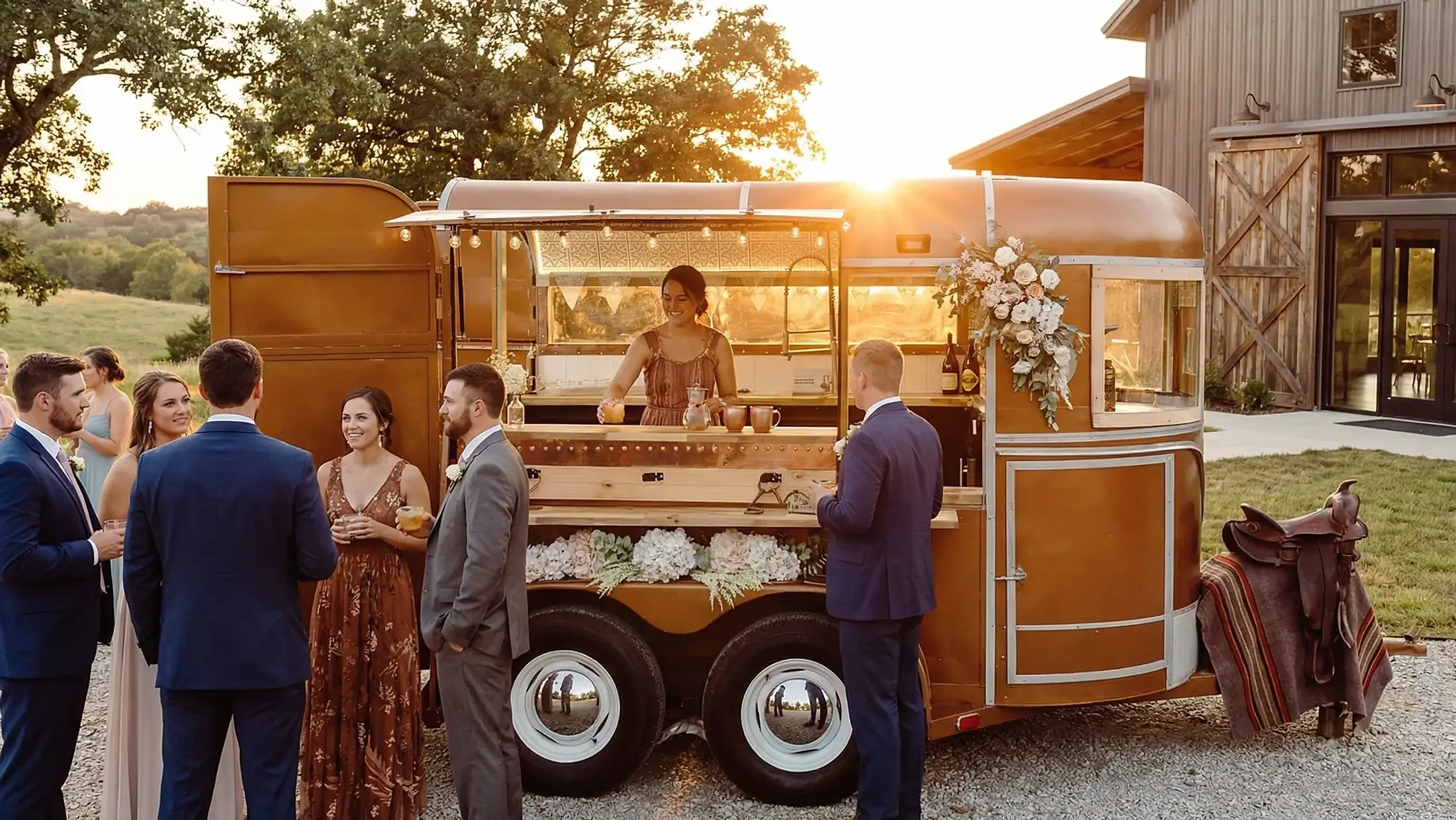 A bride and wedding guests gathered at the Steel Pony horse-trailer bar at golden hour