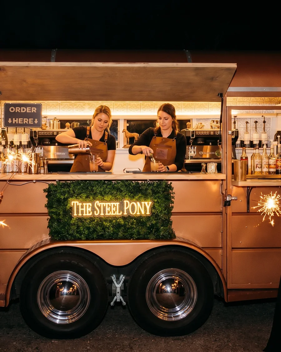 Guests raising sparklers around the Steel Pony trailer bar at a wedding